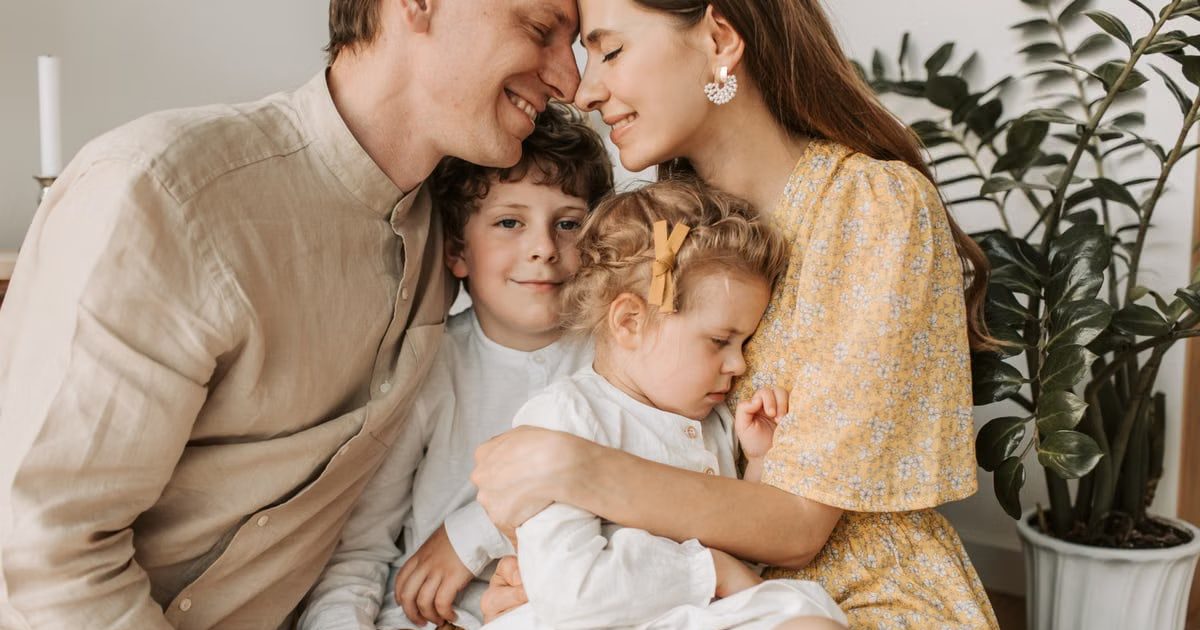 A loving family of four shares a tender moment in a cozy indoor setting, embracing and smiling.